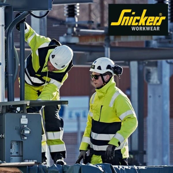 Two workers in Snickers ProtecWork hi-vis flame retardant workwear performing electrical work at height with safety helmets and protective gloves.