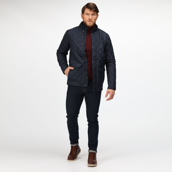Man wearing a dark quilted jacket, red shirt, and dark jeans on a white background.