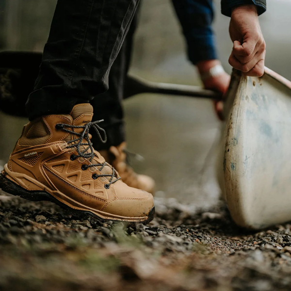 Person wearing brown work boots with a blurred background outdoors.