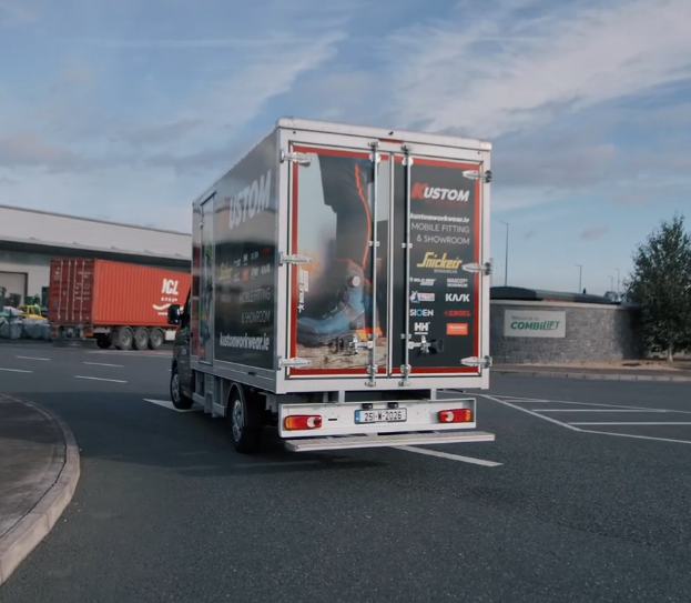 Kustom Workwear mobile fitting showroom van driving on site displaying branded livery and workwear brand logos on the rear doors.