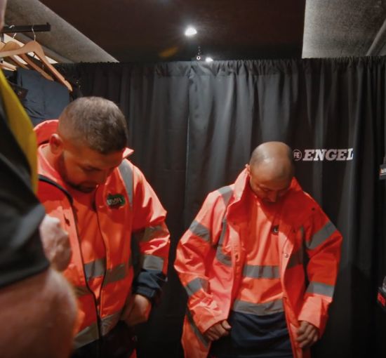 Two workers trying on hi-vis orange jackets during an on-site workwear fitting session inside the Kustom Workwear mobile fitting showroom.